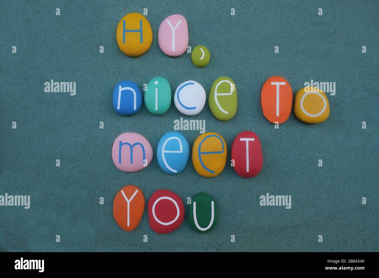 HY, piacevole per incontrarvi, testo creativo composto da lettere di pietra multicolore su sabbia verde Foto Stock