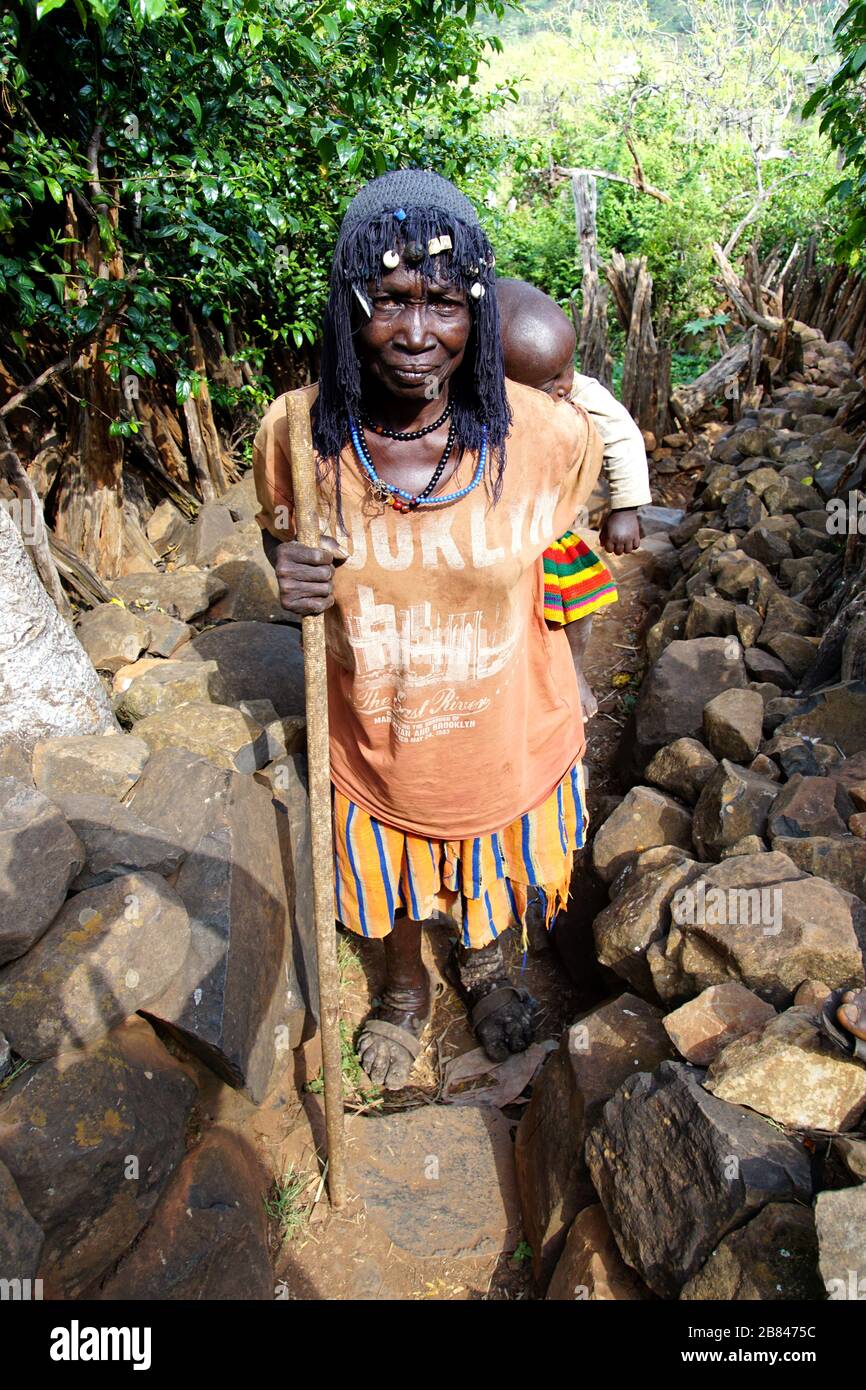 Donna del Konso locale con un bambino sulla schiena su una passeggiata attraverso il villaggio murato di Gamole Foto Stock