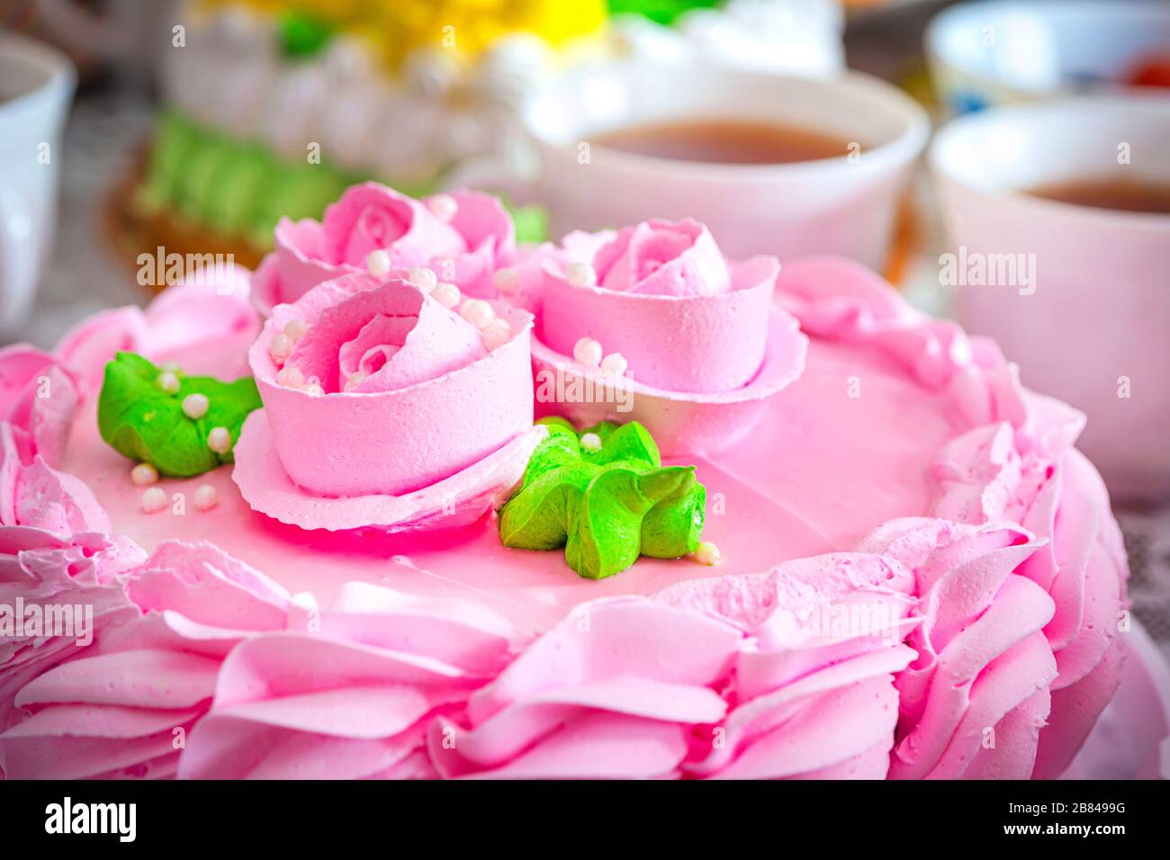 bella torta color crema rosa sullo sfondo delle tazze da tè. Tè serale con dolci. Rose e crema sulla torta. Foto Stock