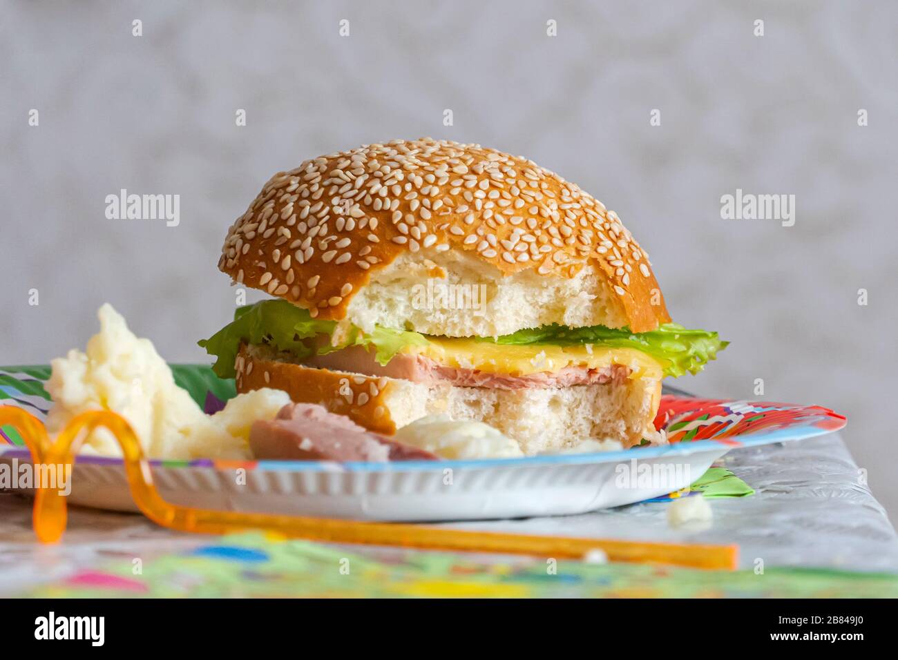 Hamburger con boccone da asporto. Panino metà-mangiato sul tavolo. Rifiuto da alimenti nocivi. Foto Stock