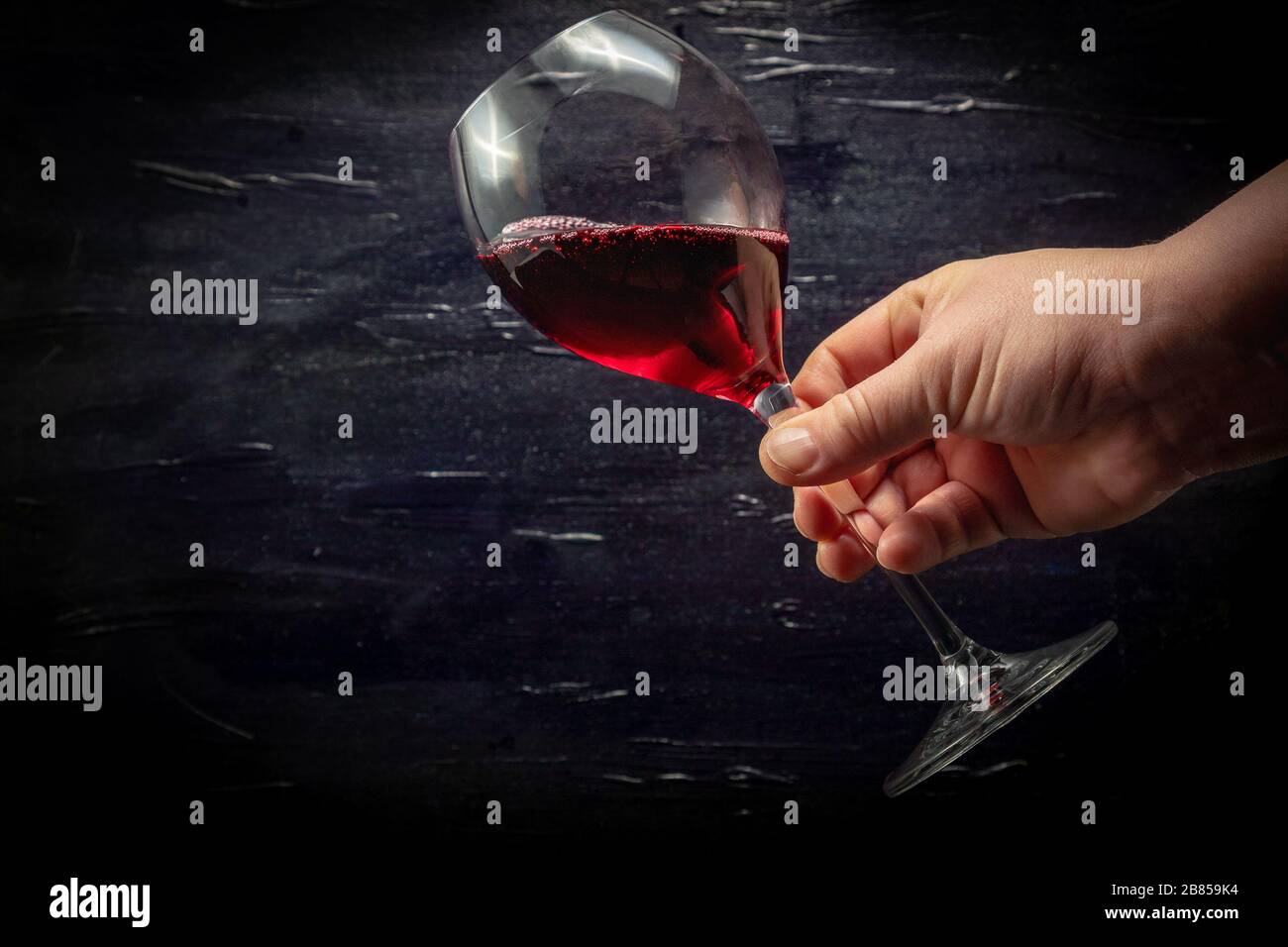 Una mano che tiene un bicchiere di vino rosso. Sfondo nero. Foto Stock