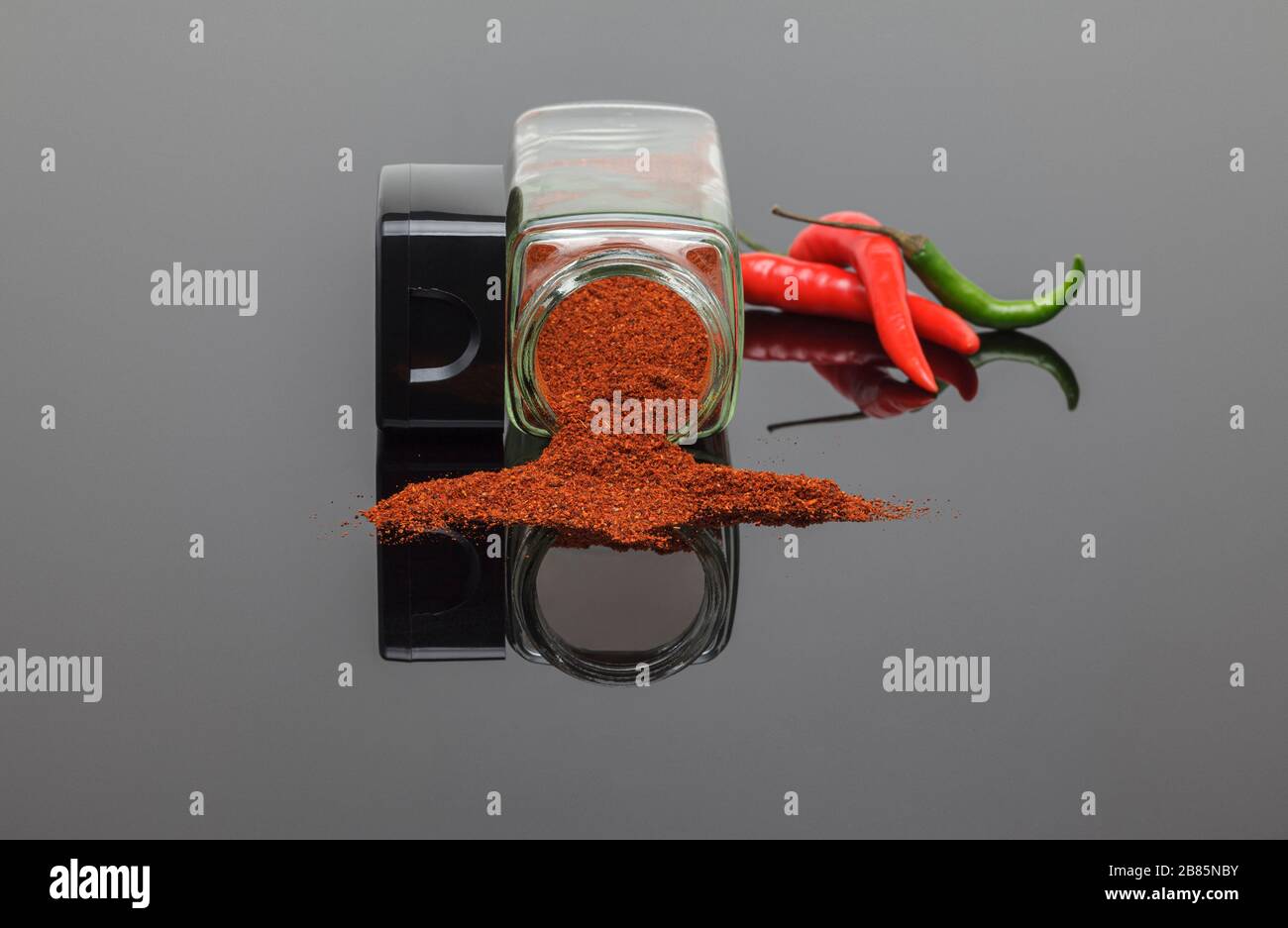 Polvere di peperoncino caldo che si versa fuori dal vaso di spezie con peperoncino fresco Foto Stock