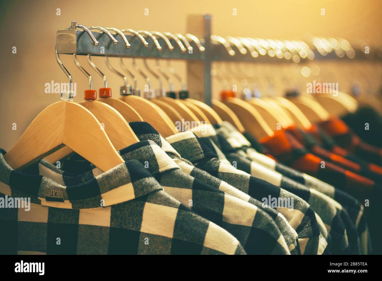 Nel negozio di abbigliamento, le camicie a scacchi di moda nei colori bianco e rosso di diverse dimensioni pendono sugli appendiabiti, illuminati dalla luce. Foto Stock