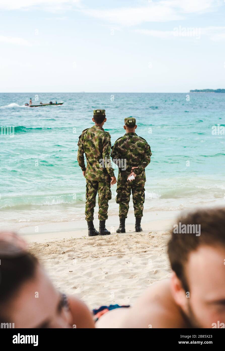 Due uomini d'esercito in uniforme camouflage guardare barche e pattuglia sulla spiaggia di Isla Baru, vicino Cartagena, Colombia Foto Stock