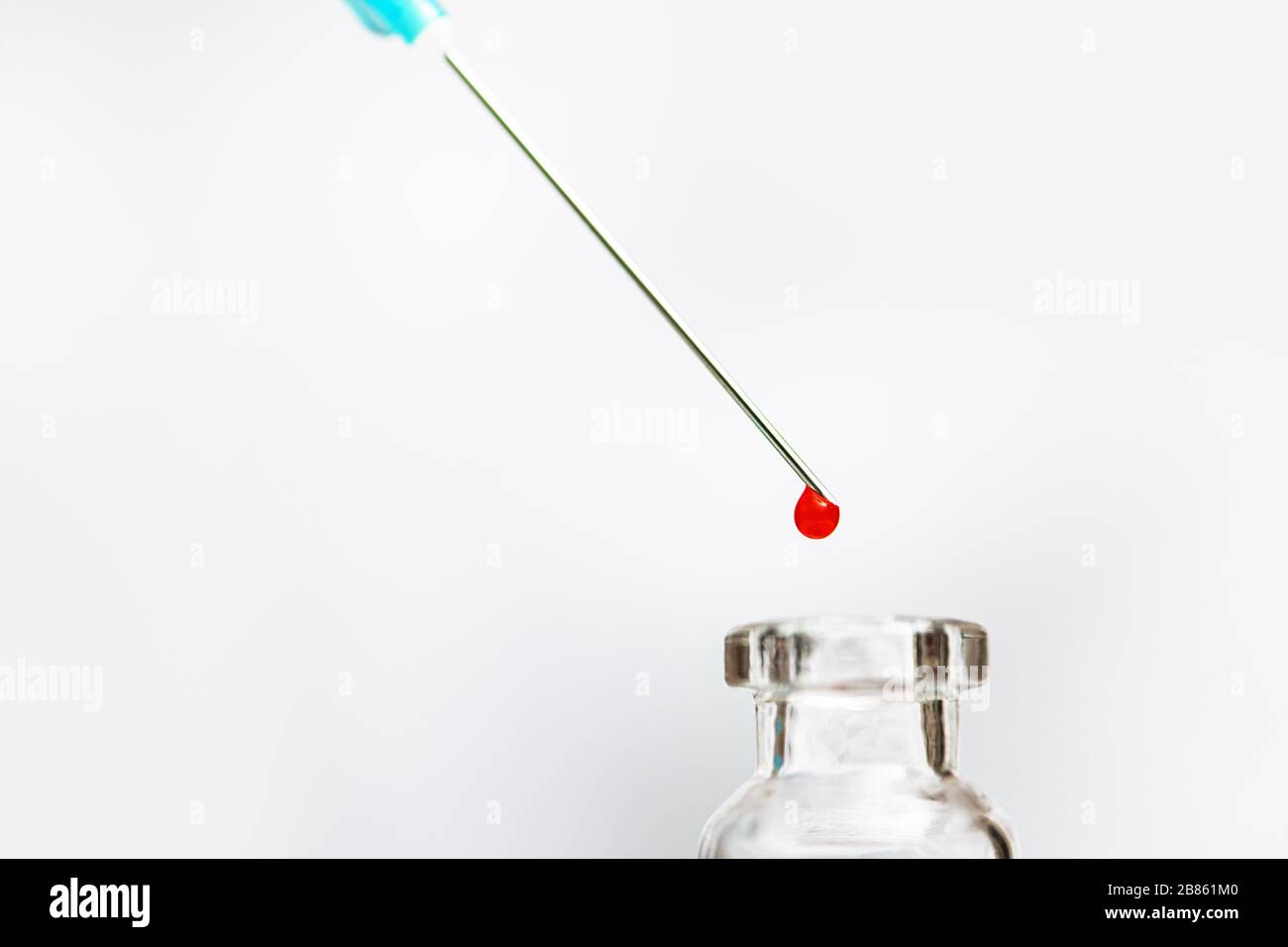 Flaconcino e ago della siringa con una goccia di liquido rosso. Foto Stock