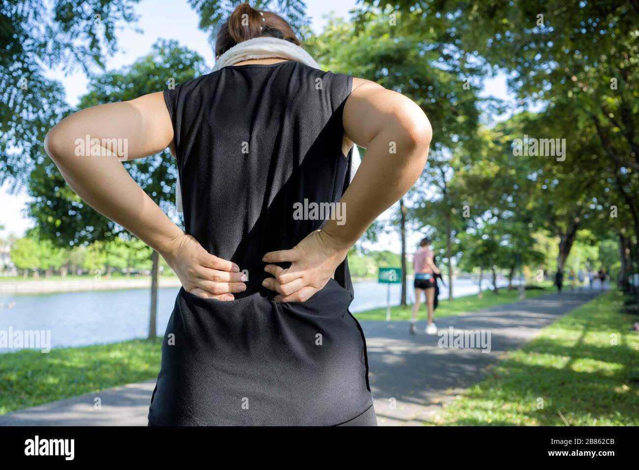 Concetto di mal di schiena. Una donna che corre con una lesione alla schiena in una tuta sportiva, tocca il muscolo inferiore della schiena che si trova sul sentiero che cattura t Foto Stock