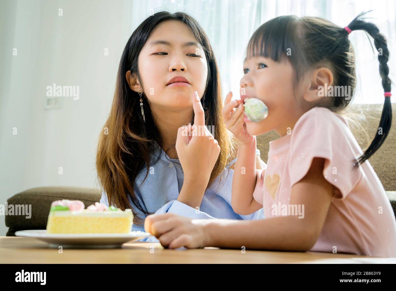 Sorelle e sorelle asiatiche, sono felici di mangiare torte. Il posto nel soggiorno ha un divano e un tavolo centrale. Foto Stock