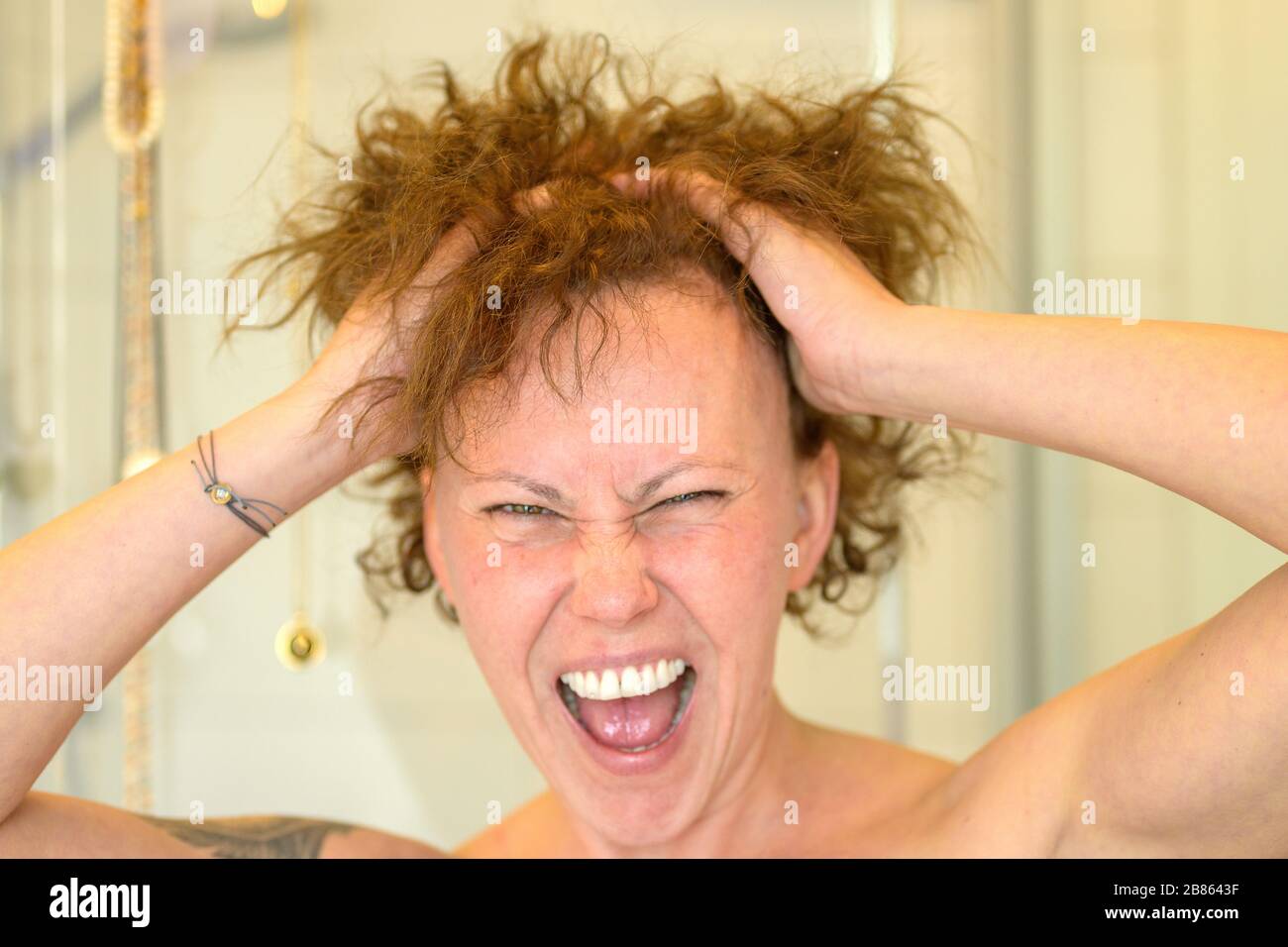 Donna frustrata che ha una giornata di capelli cattivi che le corre le mani attraverso i suoi capelli incurvati e urlando in un colpo di testa da vicino Foto Stock