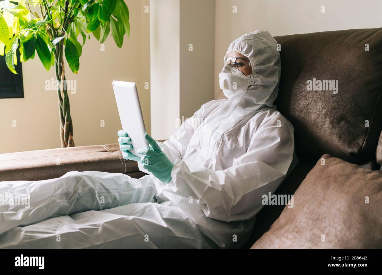 Una donna lavora da casa con il laptop, il tablet digitale e il telefono cellulare nel soggiorno, dotato di misure di sicurezza contro un virus preventio Foto Stock