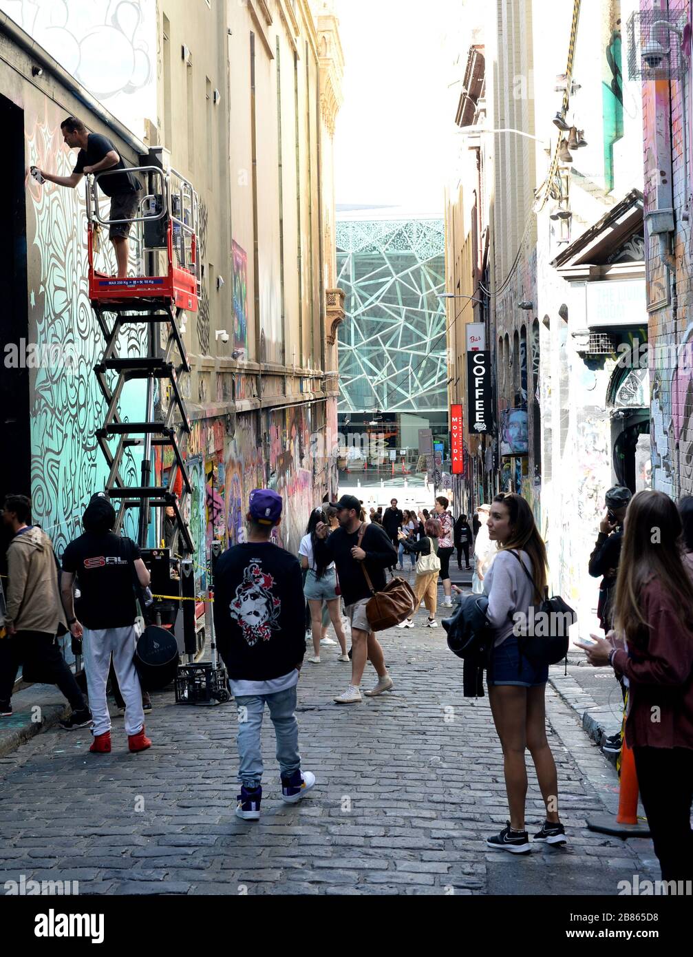 Un artista di strada lavora a Hosier Lane, Melbourne, mentre i visitatori passano sulla strada stretta piena di graffiti Foto Stock