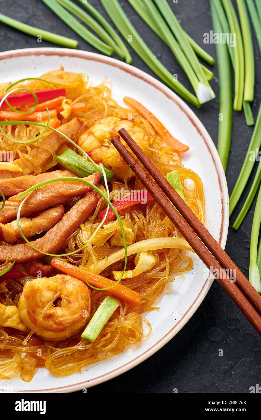 Singapore Mei Fun in bianco piatto su sfondo ardesia scuro. Singapore Noodles è un piatto di cucina cinese con tagliatelle di riso, gamberi, maiale char siu, carota, Foto Stock