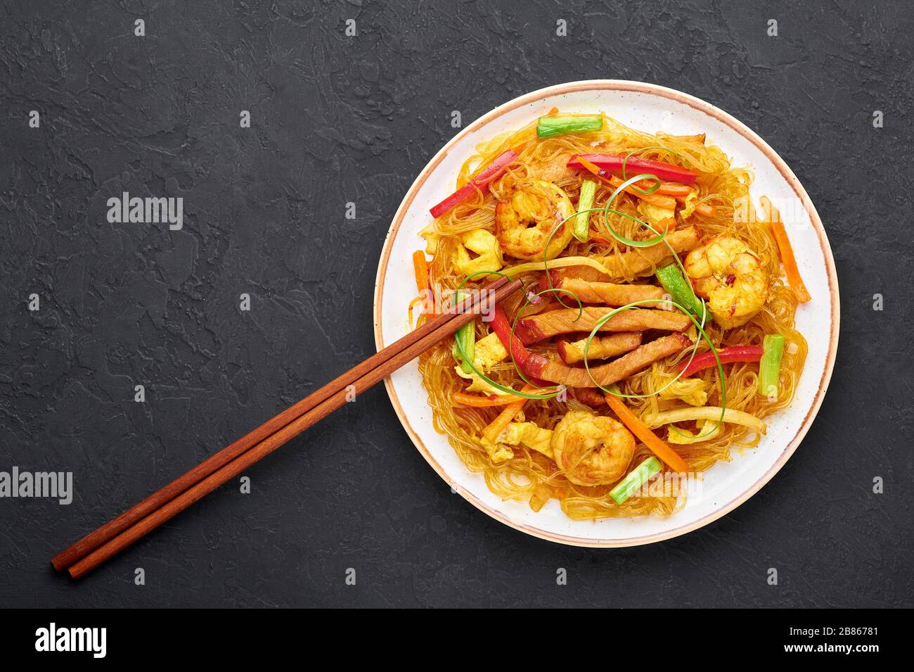 Singapore Mei Fun in bianco piatto su sfondo ardesia scuro. Singapore Noodles è un piatto di cucina cinese con tagliatelle di riso, gamberi, maiale char siu, carota, Foto Stock