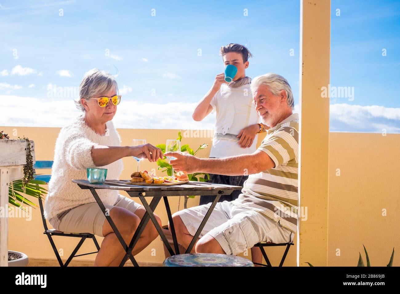 Nonni adulta e matura adolescente nipote gustare all'aperto in terrazza qualche tempo libero con cibo e bevande. oceano e vista sulla città, vacanze giornata di sole Foto Stock