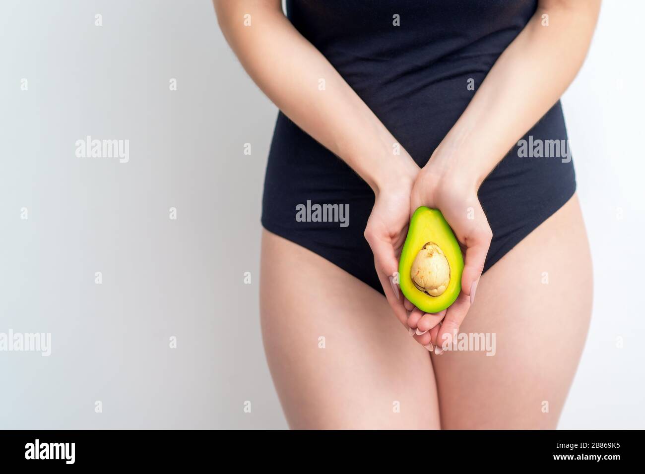 Mezzo avocado in mano di giovane donna che copre zona bikini su sfondo bianco con spazio copia. Concetto di salute degli organi intimi. Foto Stock