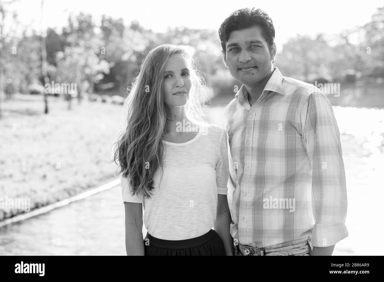 Coppia multietnica innamorata contro la splendida vista del lago al parco Foto Stock