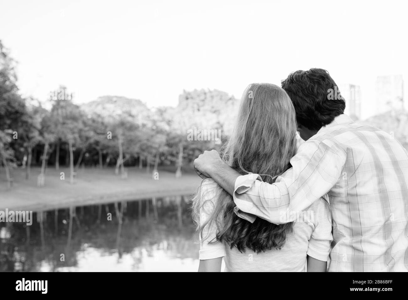 Vista sul retro di una coppia multietnica innamorata mentre si guarda al parco Foto Stock
