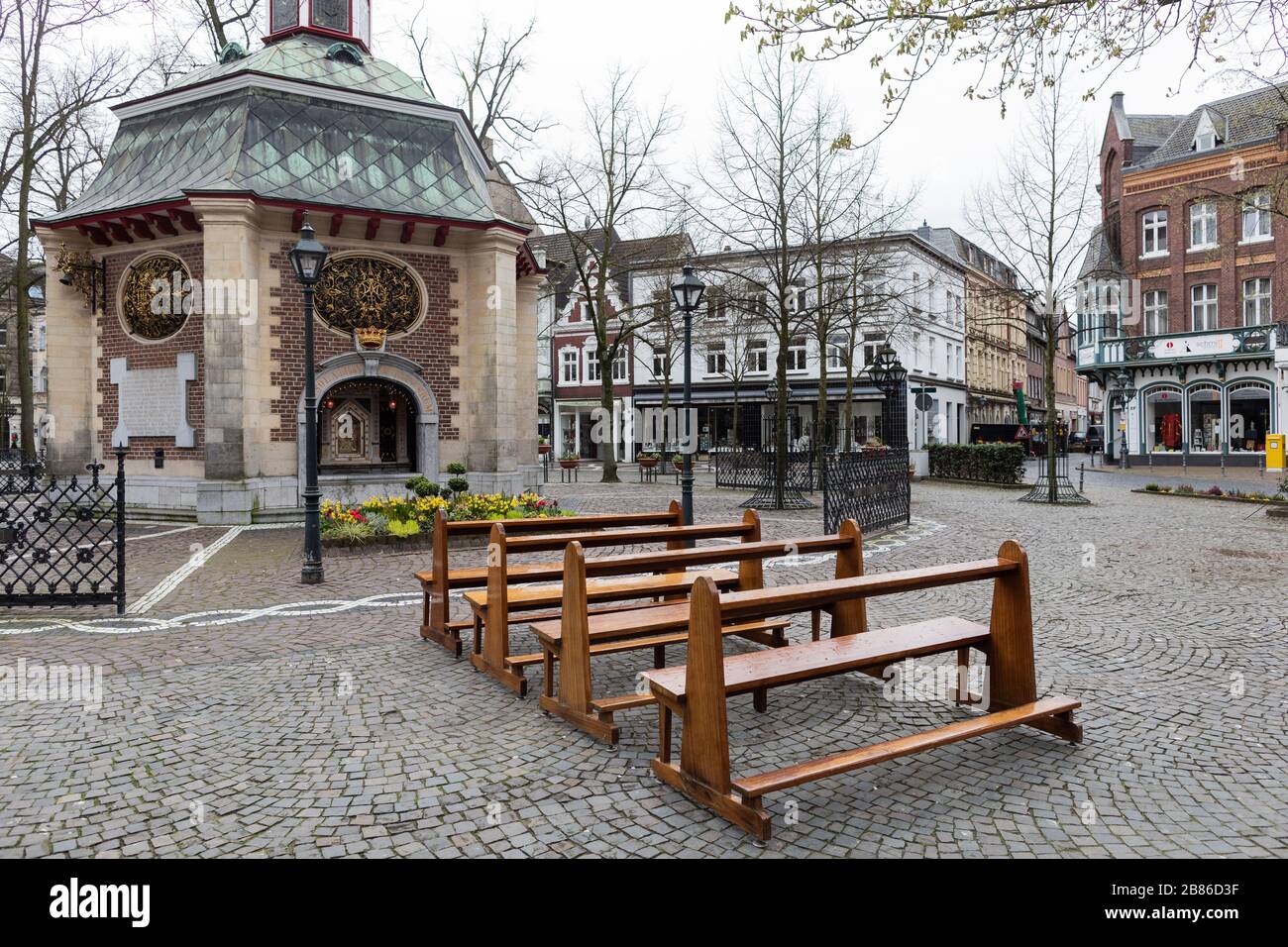 Kevelaer, Germania. 20 Marzo 2020. Panchine vuote si trovano di fronte alla Cappella della Misericordia sulla Kapellenplatz nella città di pellegrinaggio. In primo piano, la foto mostra la Madonna con un ampio mantello, sul braccio sinistro il Bambino Gesù con corona e globo, nella sua destra lo scettro, sulla sua testa una corona di stelle. Si suppone che la gente rimanga a casa a causa della diffusione del coronavirus. Credit: Rolf Vennenbernd/dpa/Alamy Live News Foto Stock