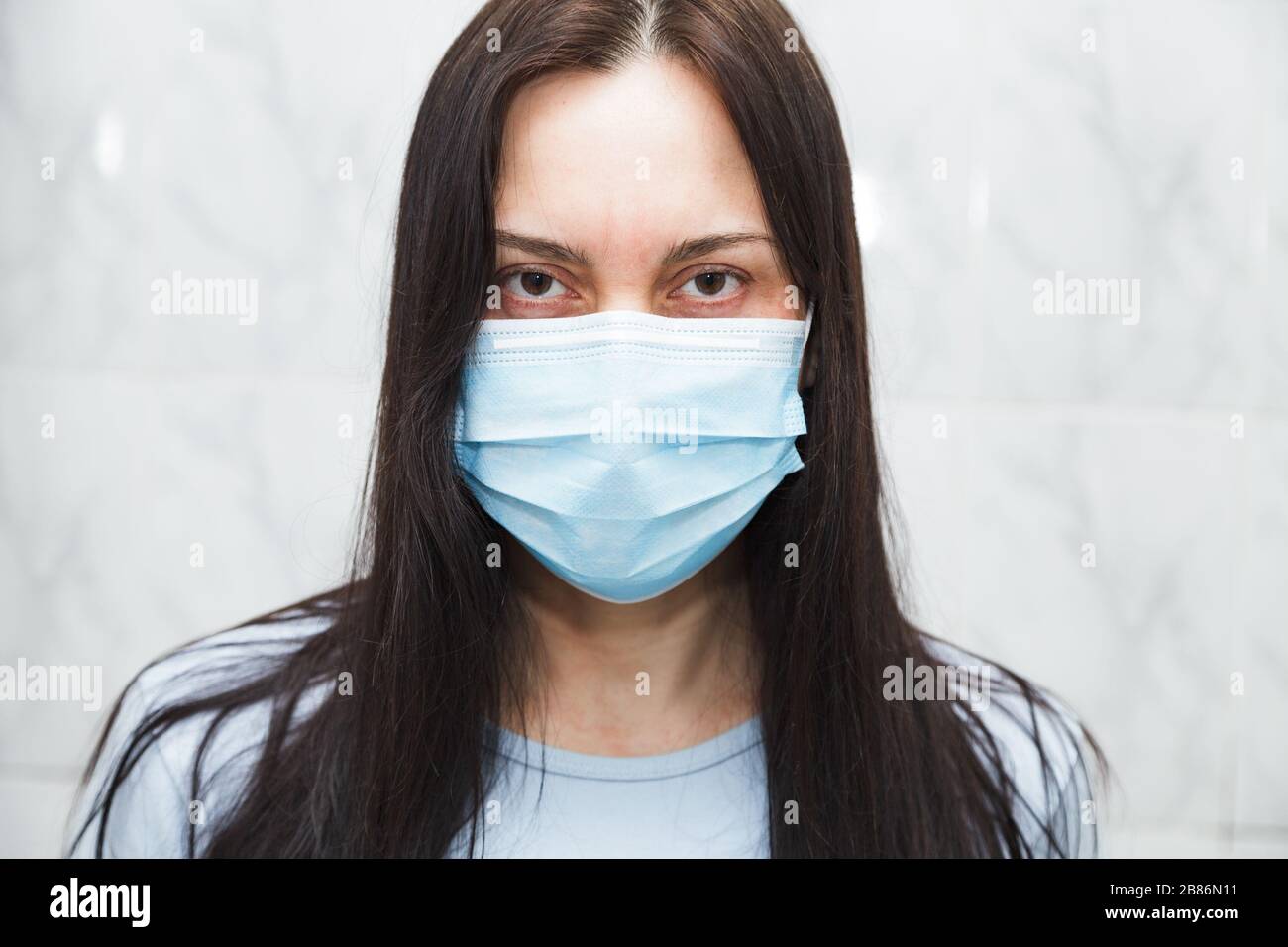 Donna in maschera medica guarda tranquillamente la macchina fotografica. Foto Stock