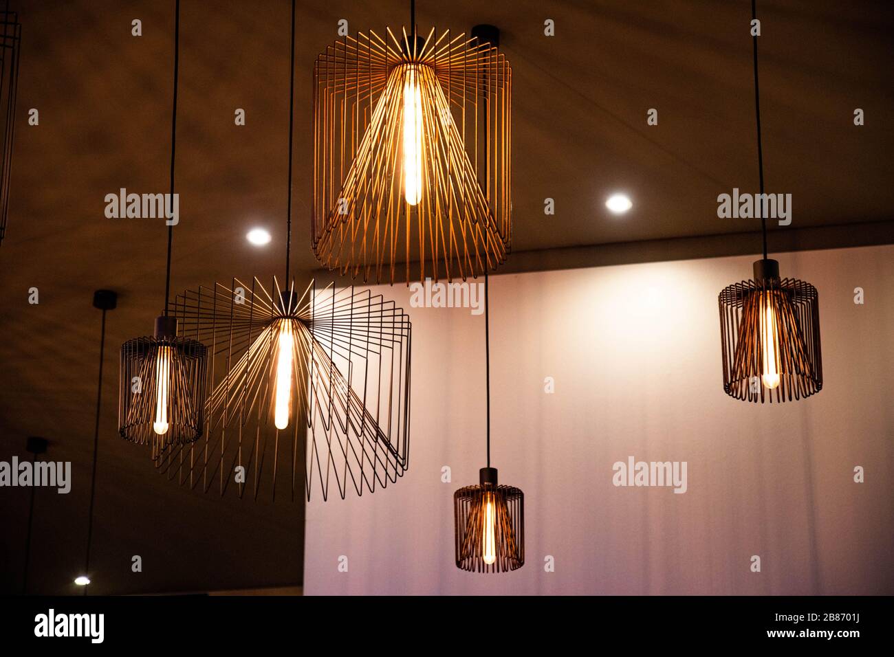 Lampadari a filo metallico geometrico di diverse dimensioni. Moderne  lampade in metallo su soffitto scuro e pareti di sfondo chiaro. Lampade con  luci luminose Foto stock - Alamy