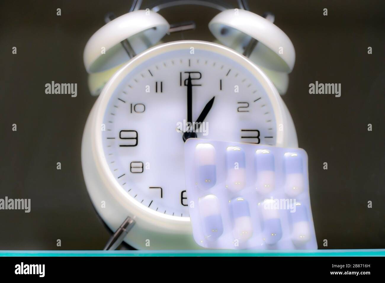 Tempo per il concetto di farmaco. Una confezione di compresse / medicine di fronte ad una tradizionale sveglia a campana, con le mani che mostrano le ore 1. Foto Stock