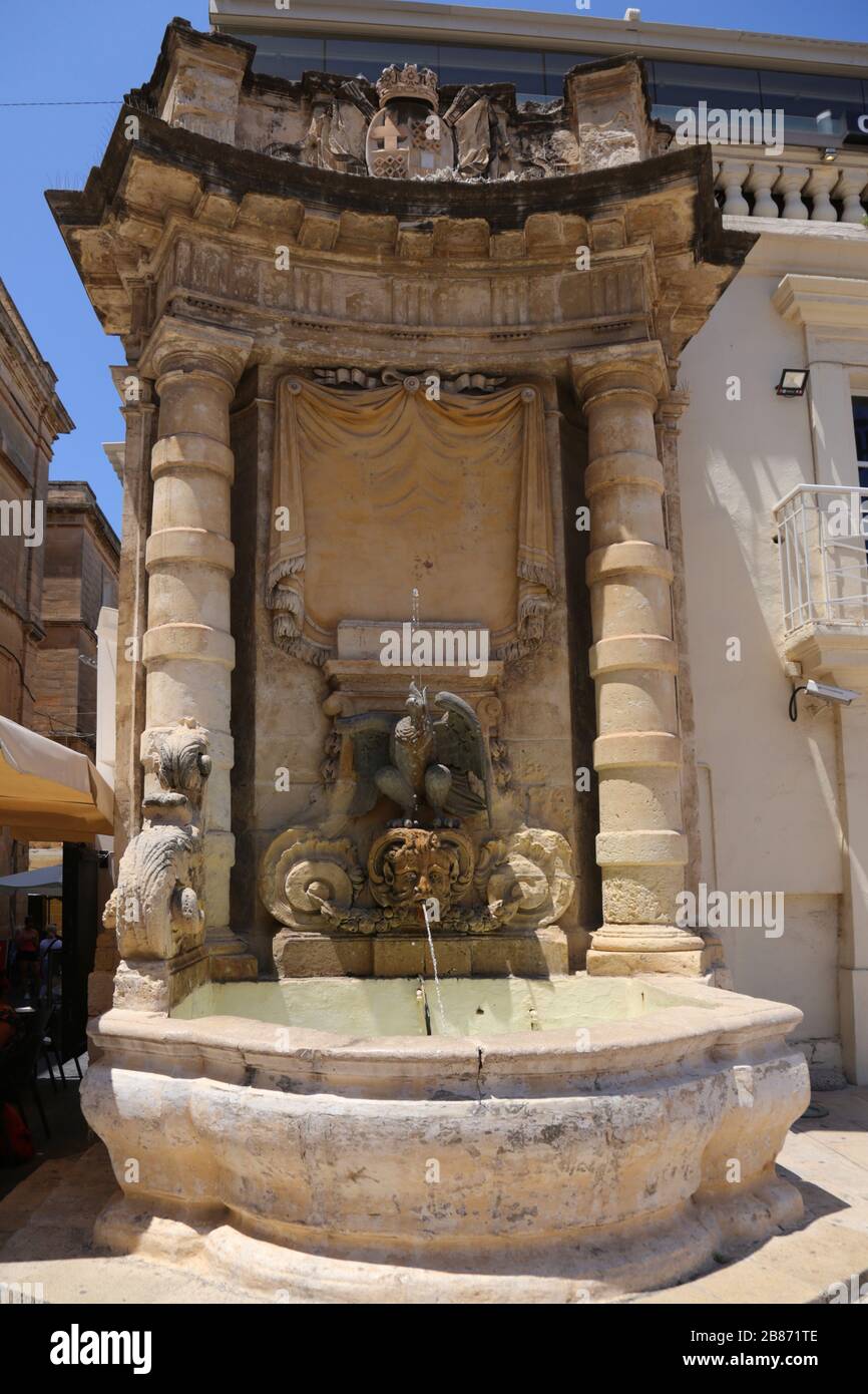 Valletta. Malta. Fontana in pietra arenaria in Piazza San Giorgio con figura dell'aquila e della testa di`s faun. Angolo dell'edificio della Vecchia Guardia Centrale. Foto Stock