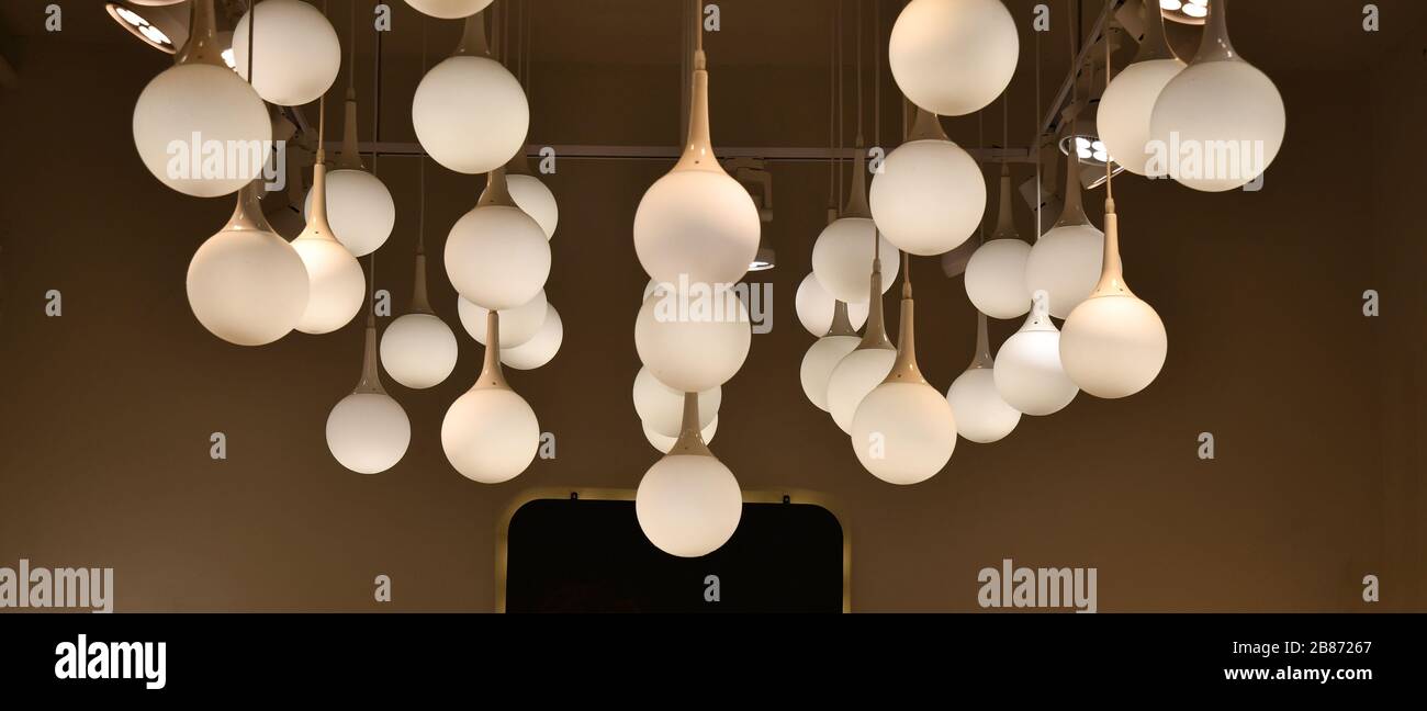Lampade a lampadina bianche di lampadario appese al soffitto. Paralumi a sfera in vetro opaco su sfondo marrone. Illuminazione interna. Foto Stock