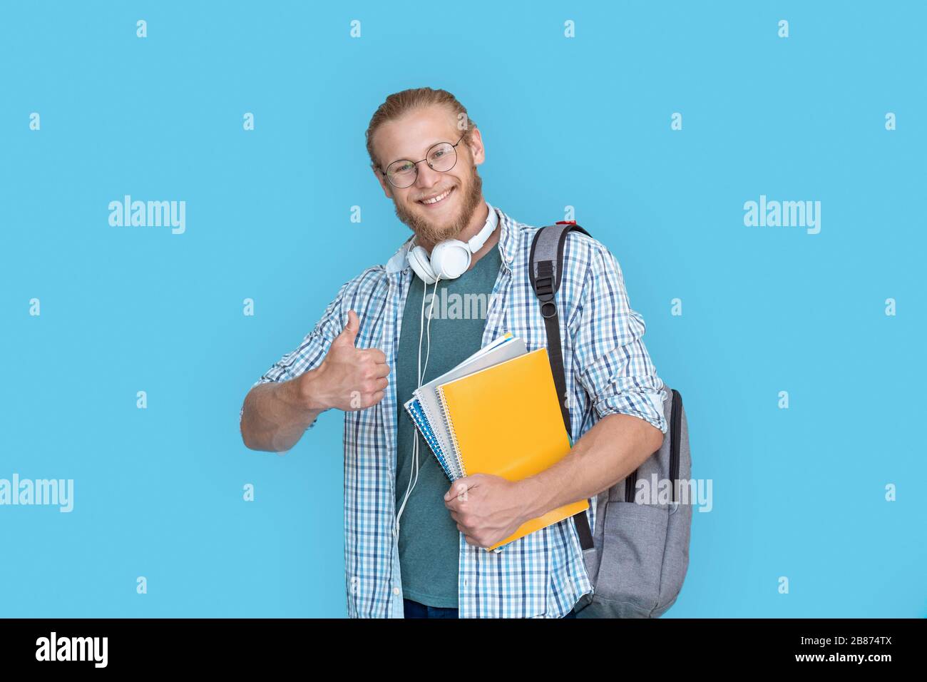 Zaino Happy maschio Student Hold che mostra pollici isolati su sfondo blu. Foto Stock