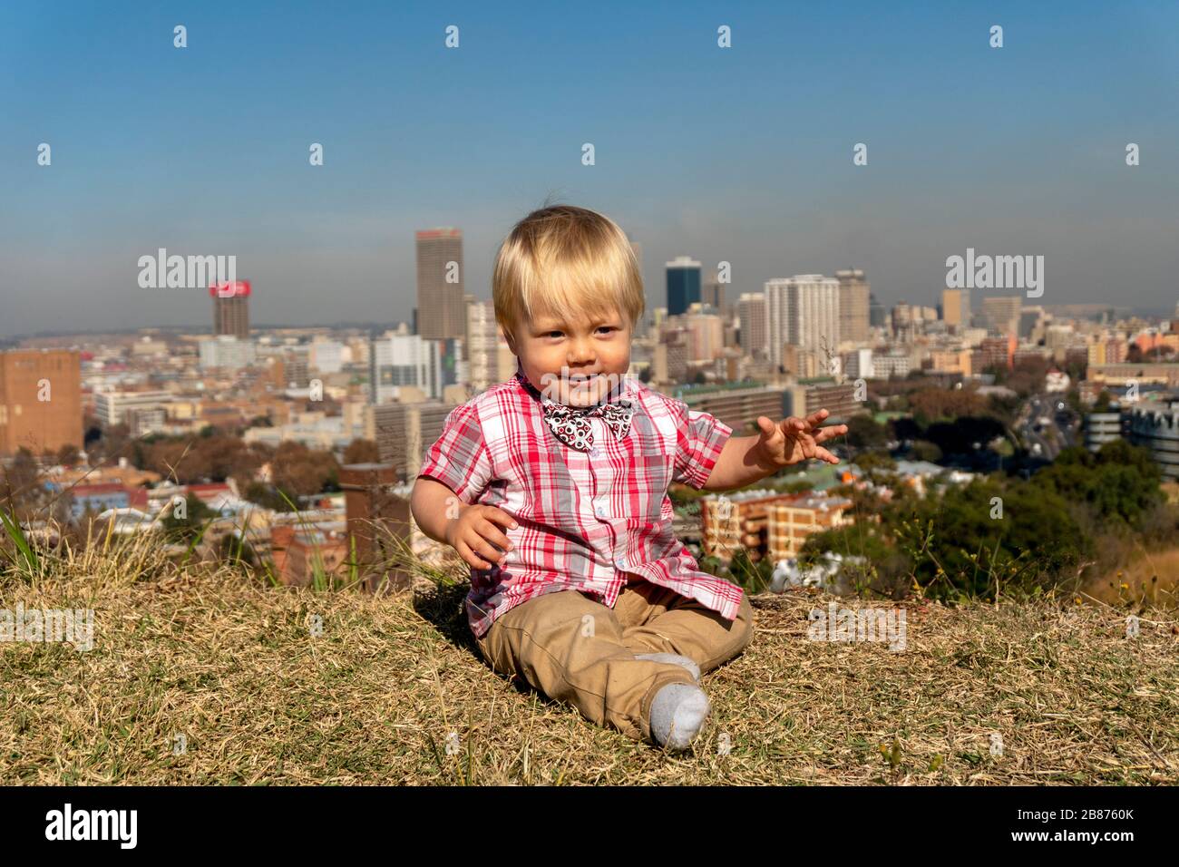 Un ragazzino che si riposa sul prato con una vista incredibile su Johannesburg, Sud Africa Foto Stock