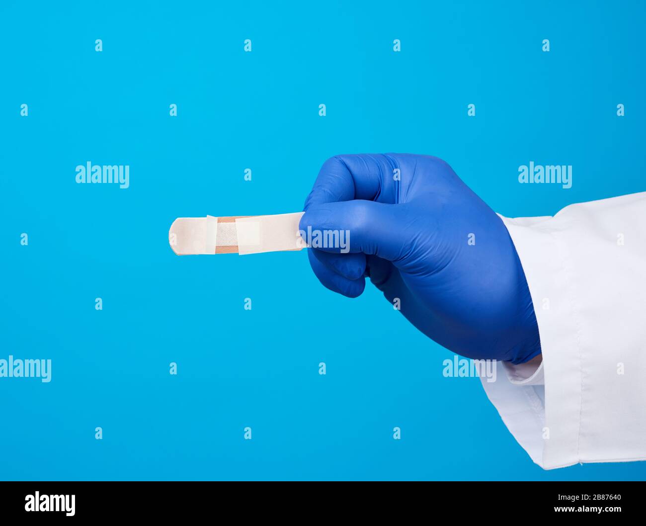 medico maschile in un cappotto bianco, guanti medici in lattice blu contiene un cerotto adesivo medico tessile, primo piano Foto Stock