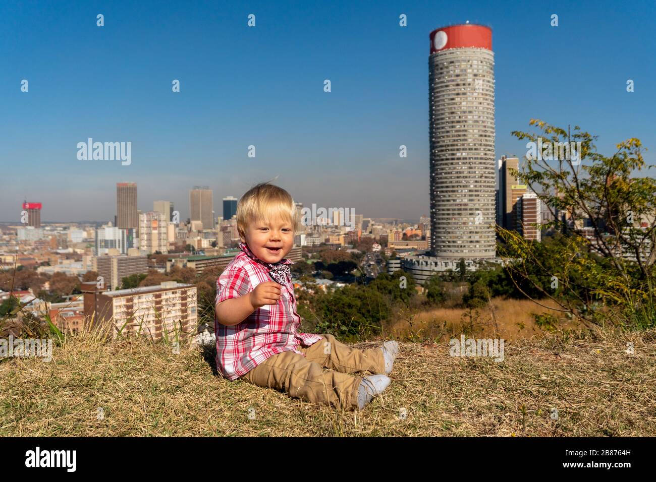 Un ragazzino che si riposa sul prato con una vista incredibile su Johannesburg, Sud Africa Foto Stock