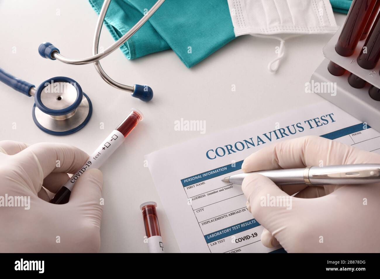 Il medico compila il modulo di analisi del coronavirus sul banco di laboratorio con campioni di sangue da analizzare. Vista dall'alto. Foto Stock