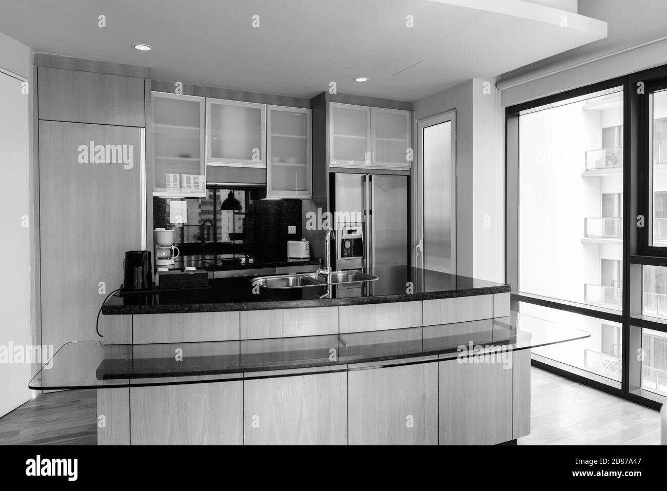 Lussuosa cucina moderna in legno e pulita con piano in vetro contro la finestra illuminata dal sole Foto Stock