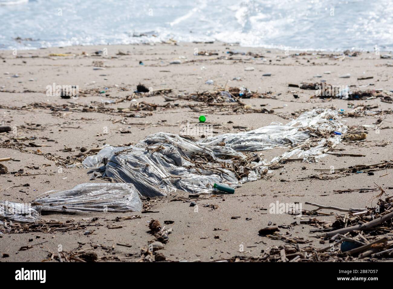 Un grosso sacco di plastica sulla fronte che inquina la spiaggia con altri rifiuti provenienti da esseri umani. Il mare è sullo sfondo. Foto Stock