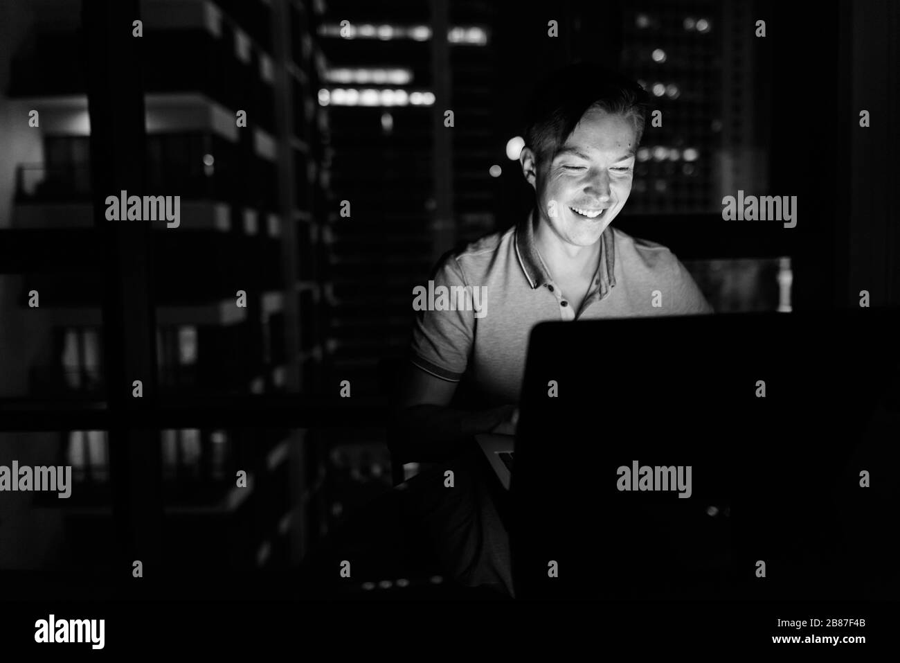 Giovane bell'uomo che usa il laptop contro la vista della città di notte Foto Stock