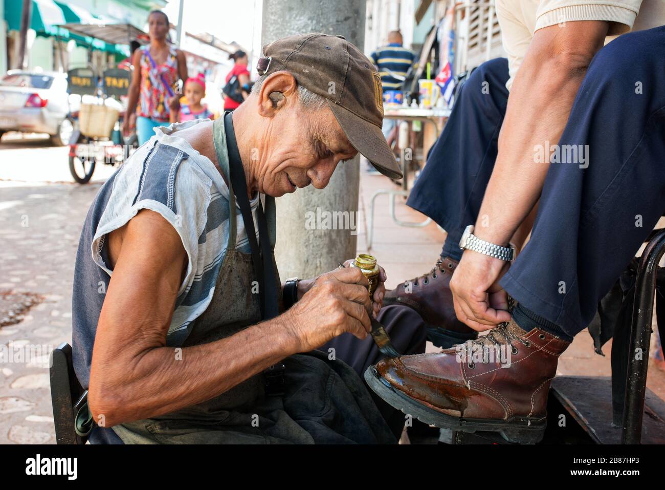 Lustrascarpe da strada. Uomo con una moneta nell'orecchio fotografato mentre pulisce le scarpe di un cliente. Foto Stock