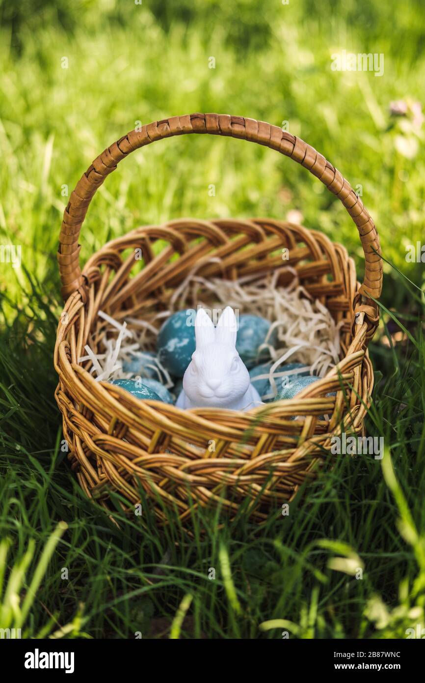Uova di pasqua dipinte blu testurizzate e un coniglio di plastica bianco in un cestino fatto a mano marrone vimini su erba fresca verde. Il concetto di holida di primavera Foto Stock