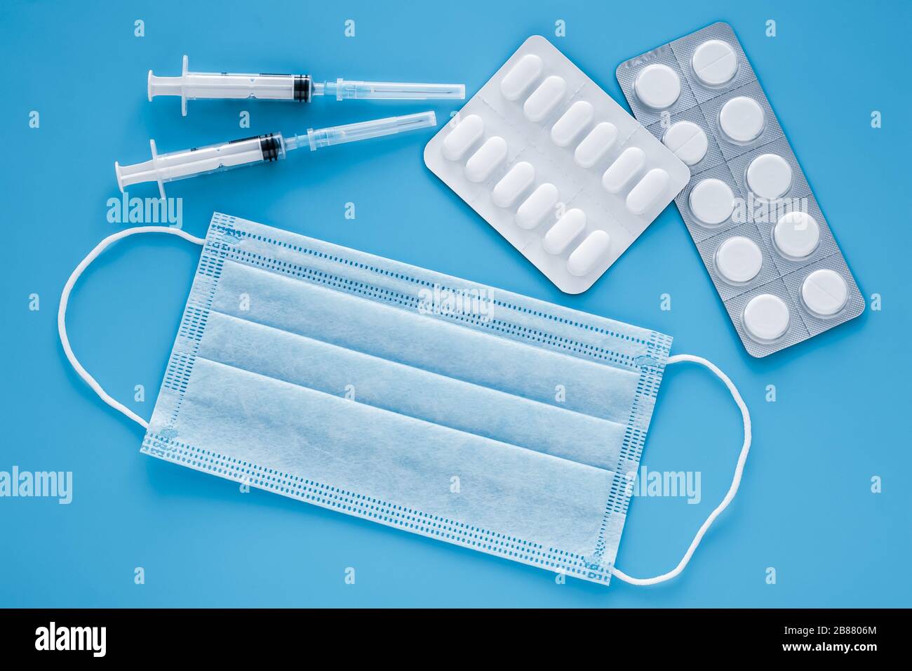 Maschera medica protettiva, pillole e due siringhe su sfondo blu. Concetto di medicina, quarantena. Sfondo blu Foto Stock