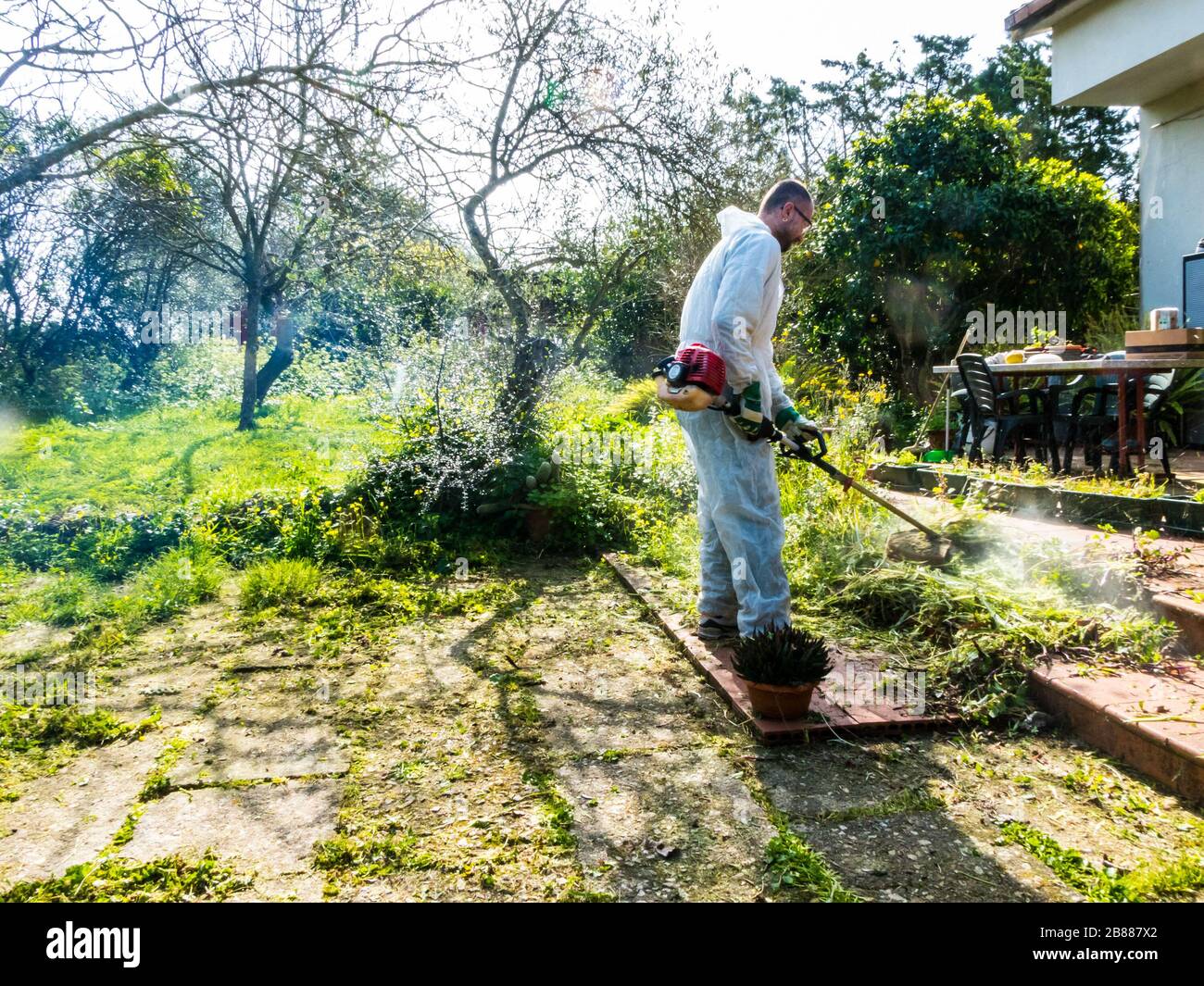 Uomo che indossa una tuta bianca tagliando l'erba in giardino in una giornata di sole Foto Stock