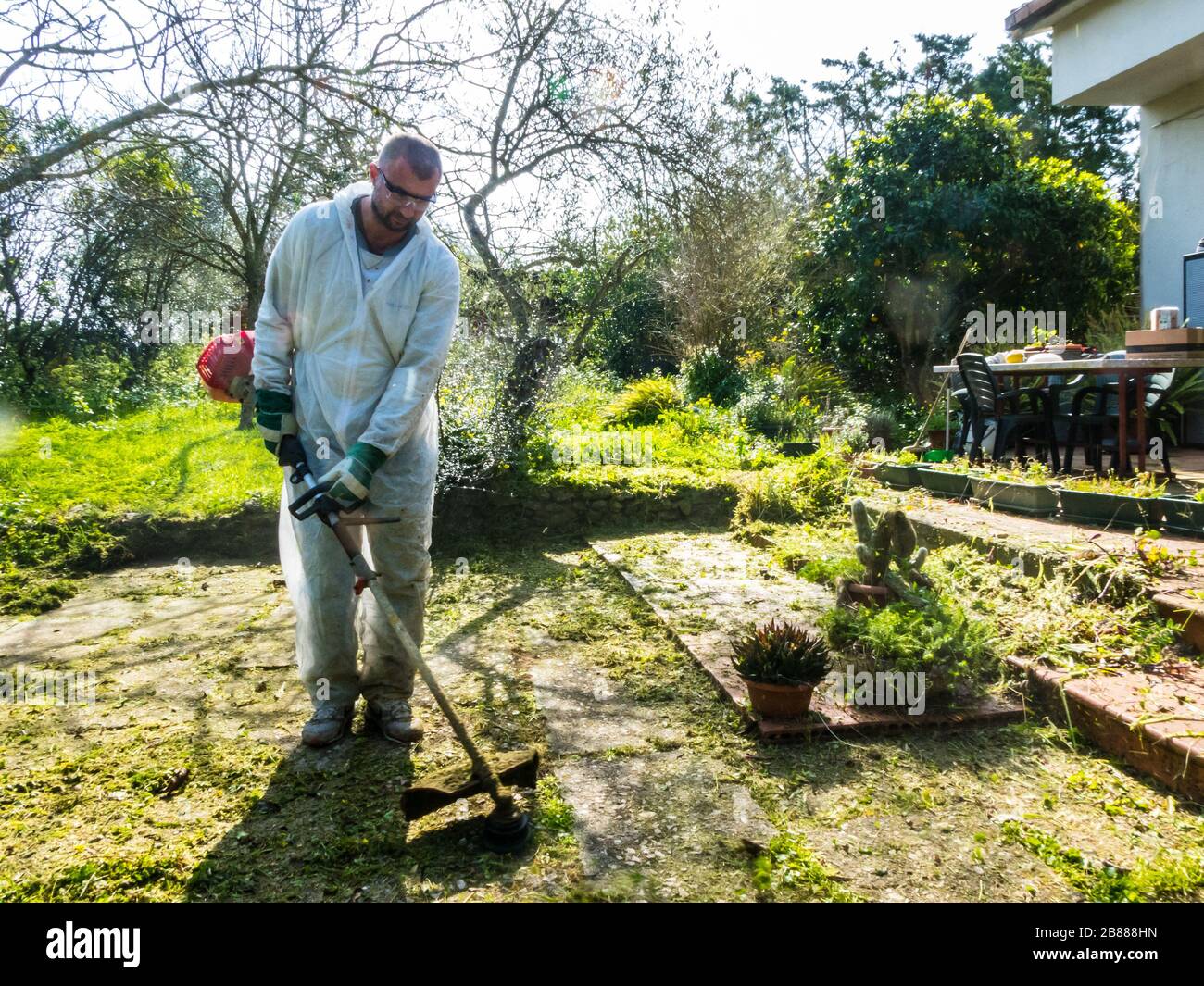 Uomo che indossa una tuta bianca tagliando l'erba in giardino in una giornata di sole Foto Stock