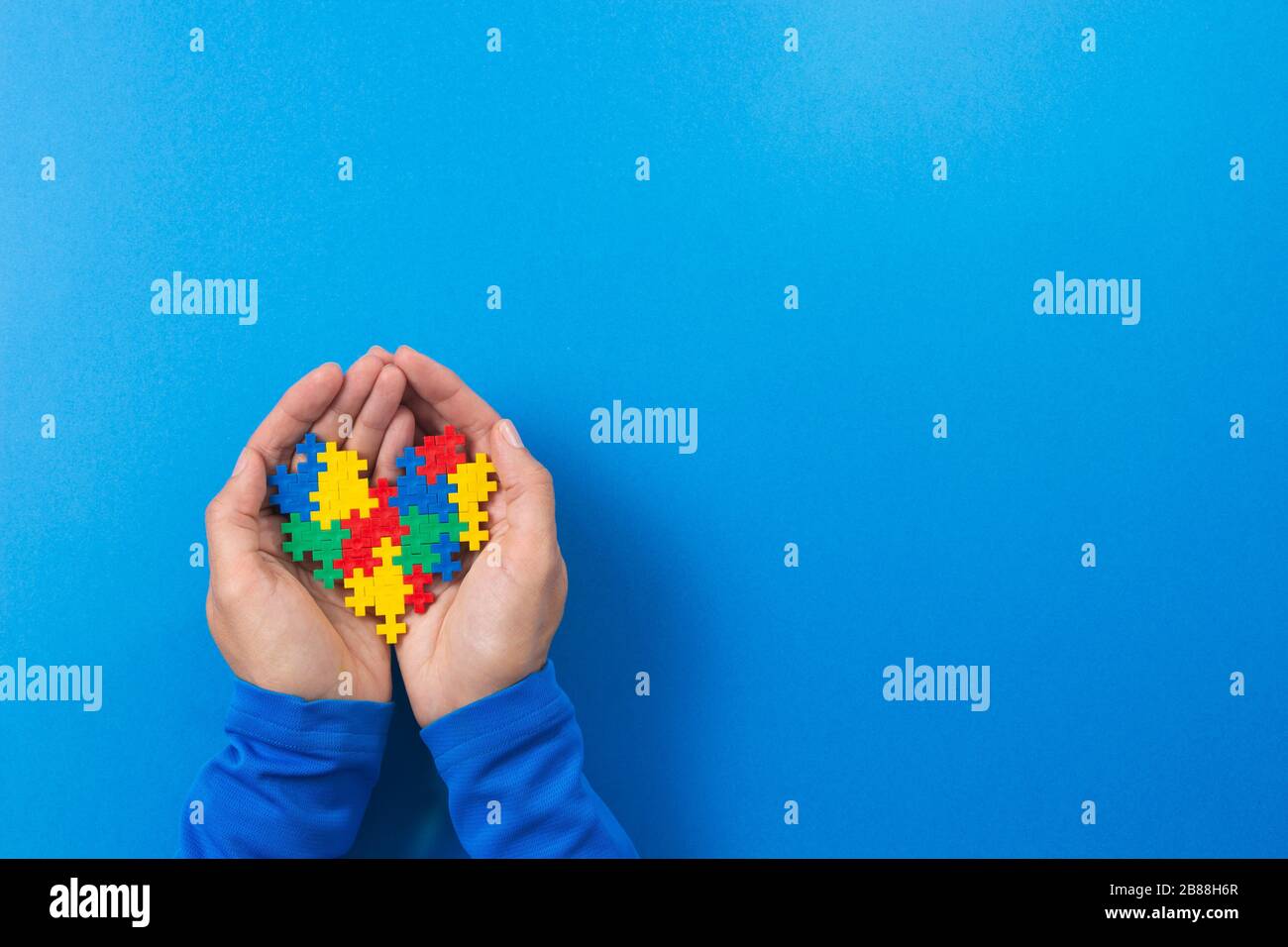 Concetto del giorno di consapevolezza di autismo del mondo. Le mani del bambino tengono il cuore colorato del puzzle su sfondo blu Foto Stock