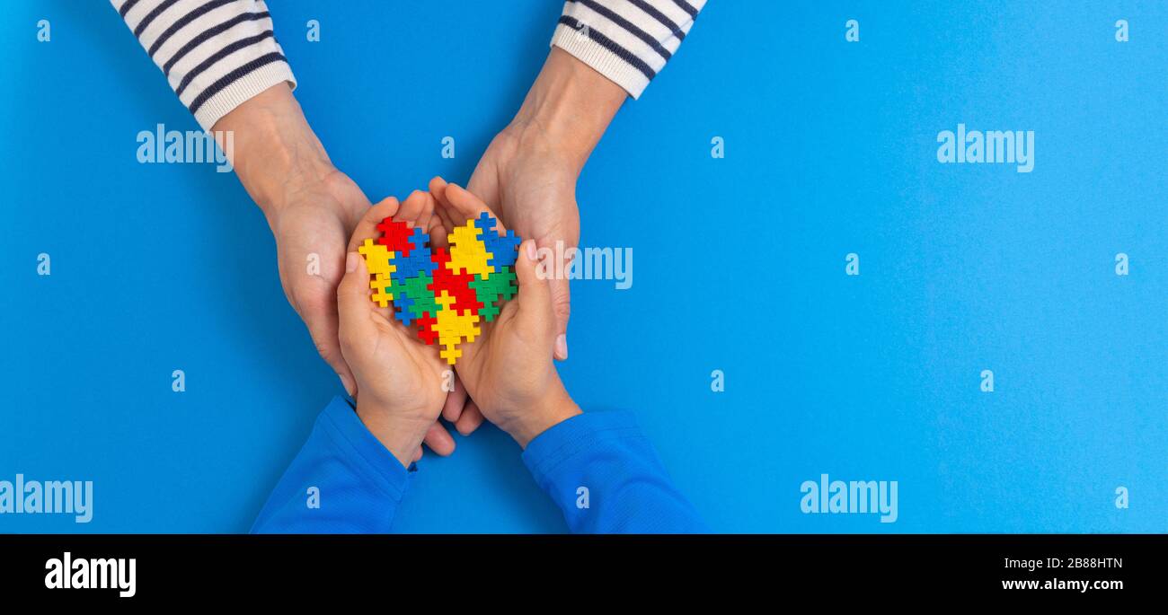 Concetto del giorno di consapevolezza di autismo del mondo. Donna e bambino mani tenendo puzzle cuore su sfondo azzurro Foto Stock