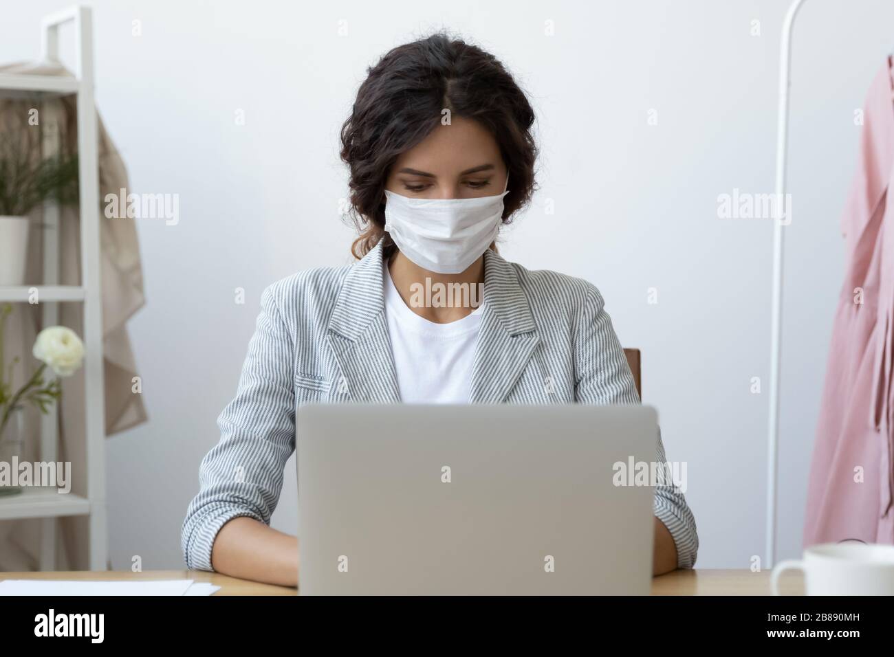 Donna d'affari in maschera che lavora su un computer portatile seduto alla scrivania del posto di lavoro Foto Stock