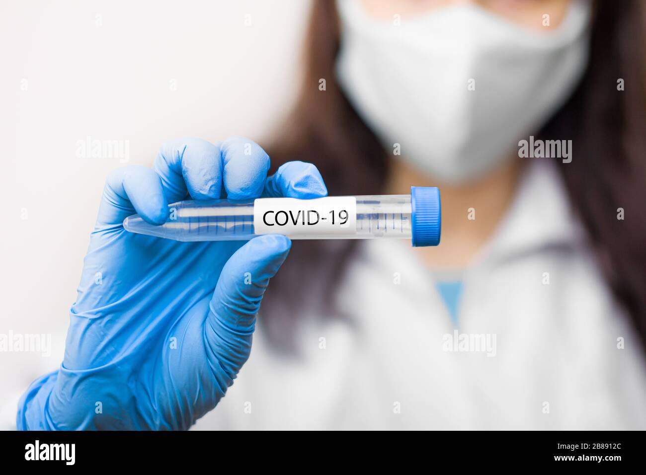 Provetta con vaccino contro il coronavirus, 2019-nCoV, SARS-nCov, COVID-19 in maschera protettiva e guanti blu per scienziato. Foto Stock