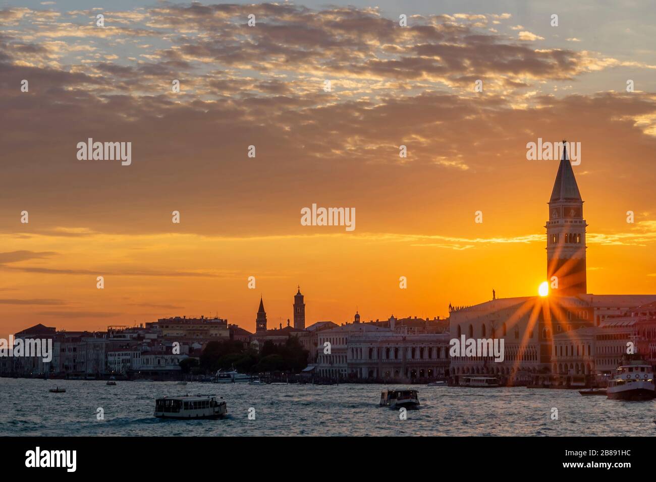 Tramonto colorato sul centro storico di Venezia, Italia, con raggi di sole che filtrano dal Campanile di San Marco sopra il Palazzo Ducale Foto Stock