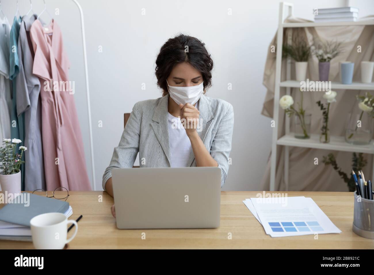 Donna d'affari malsana in maschera seduta alla scrivania e tosse Foto Stock