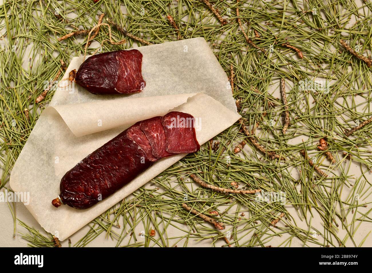 Salsiccia secca a base di caprioli. Tagliare con le fette sulla pergamena. Pavimenti in aghi di pino. Foto Stock