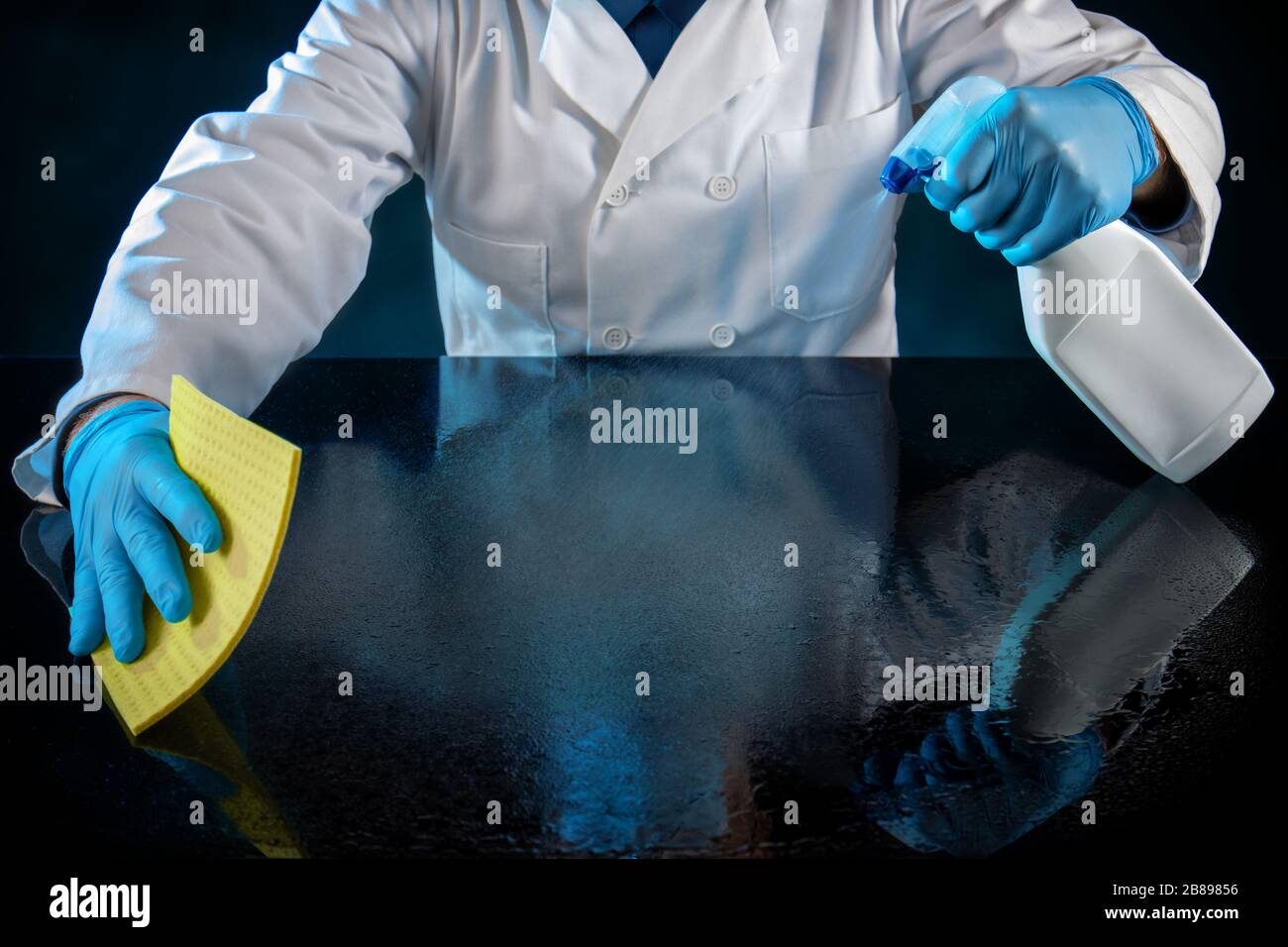 Persona vestita in uniforme bianca spruzzando un tavolo con soluzione anti virus Foto Stock