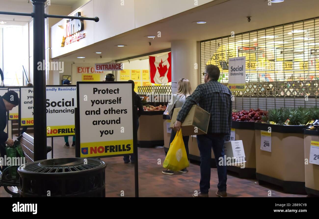 Vancouver, Canada - Mar 20,2020: Le persone si allineano per entrare No Frills Store praticando le distanze sociali tra di loro a causa di COVID-19. Foto Stock