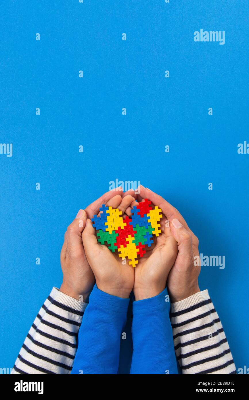 Concetto del giorno di consapevolezza di autismo del mondo. Mani per adulti e bambini che tengono il cuore del puzzle su sfondo blu chiaro Foto Stock