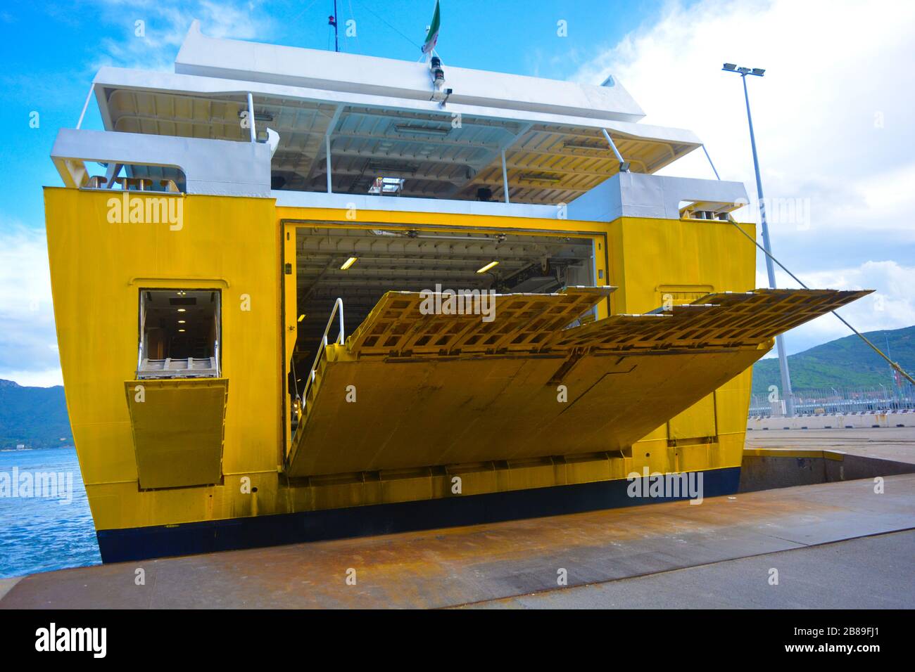 La poppa di un grande traghetto giallo che arriva al porto e si prepara per lo sbarco. La rampa sta scendendo sulla banchina del porto. Giornata tranquilla Foto Stock